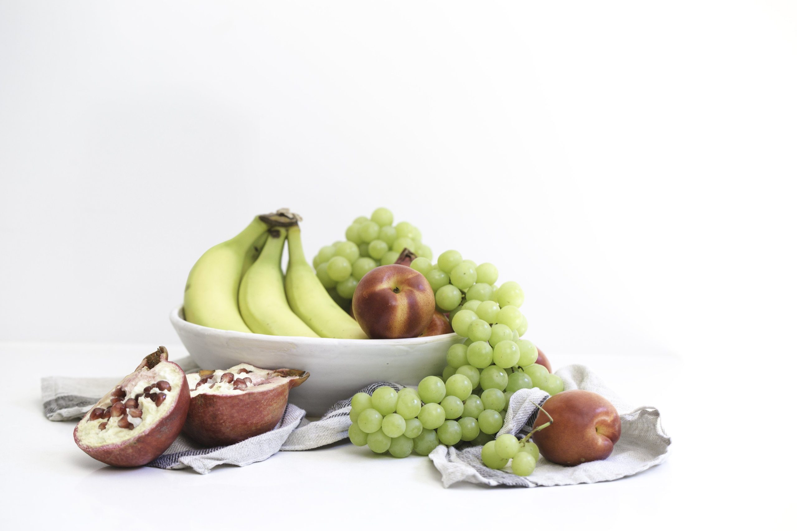 A vibrant mix of bananas, grapes, nectarines, and pomegranates in a white bowl.