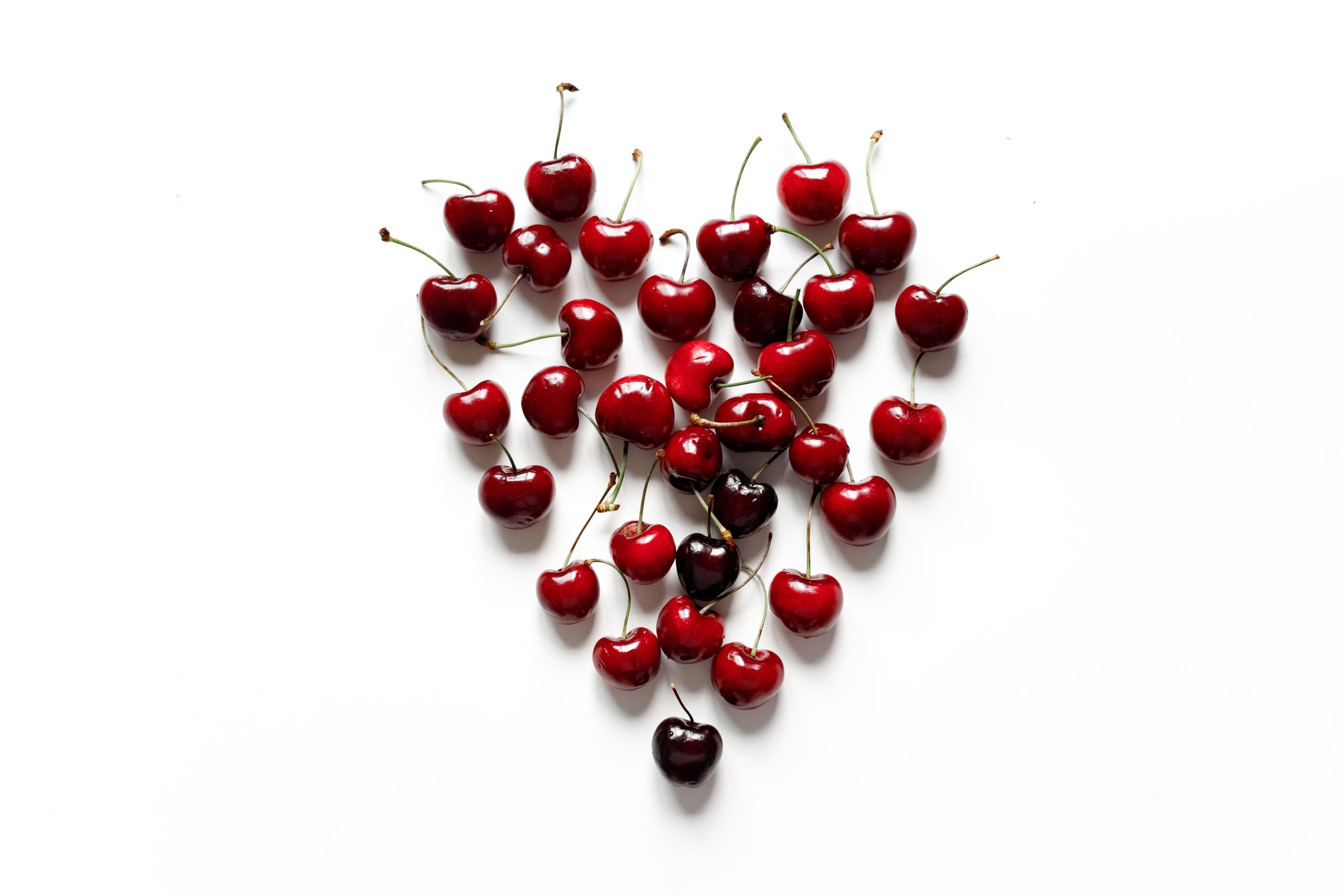Juicy red cherries arranged in a heart shape on a clean white background, perfect for healthy food concepts.