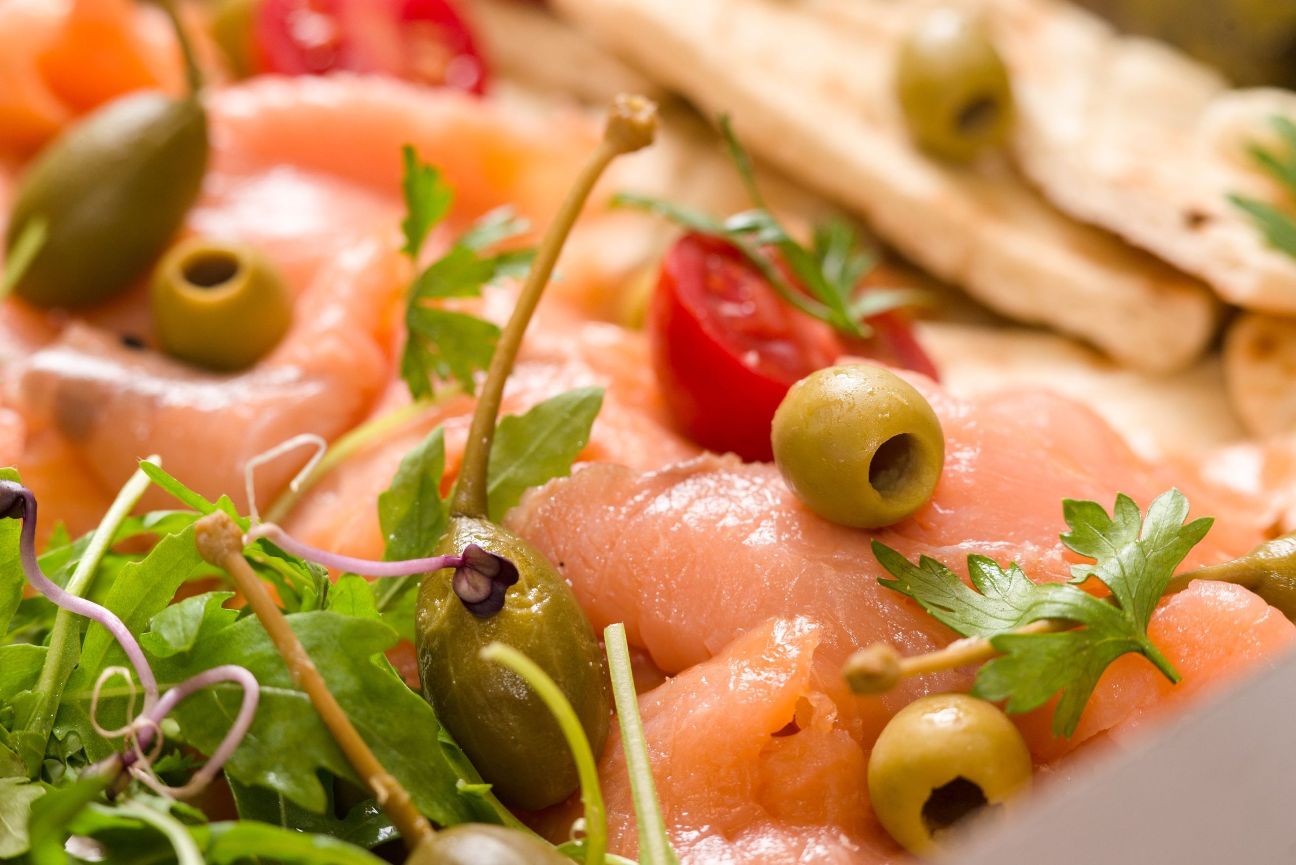A vibrant close-up of a fresh Mediterranean platter featuring salmon, olives, and greens.