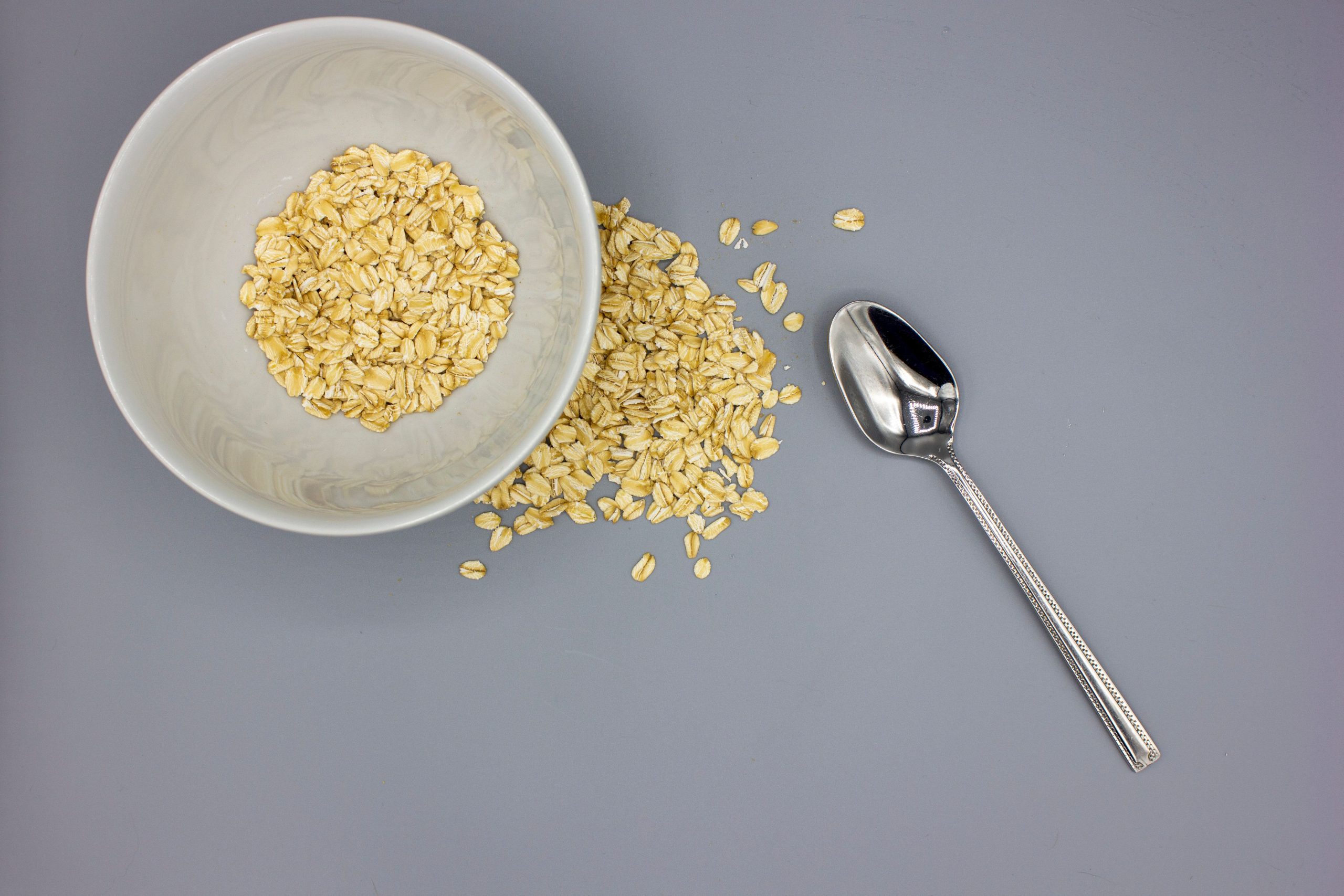 Minimalist top view of oats in bowl with a spoon on gray background.