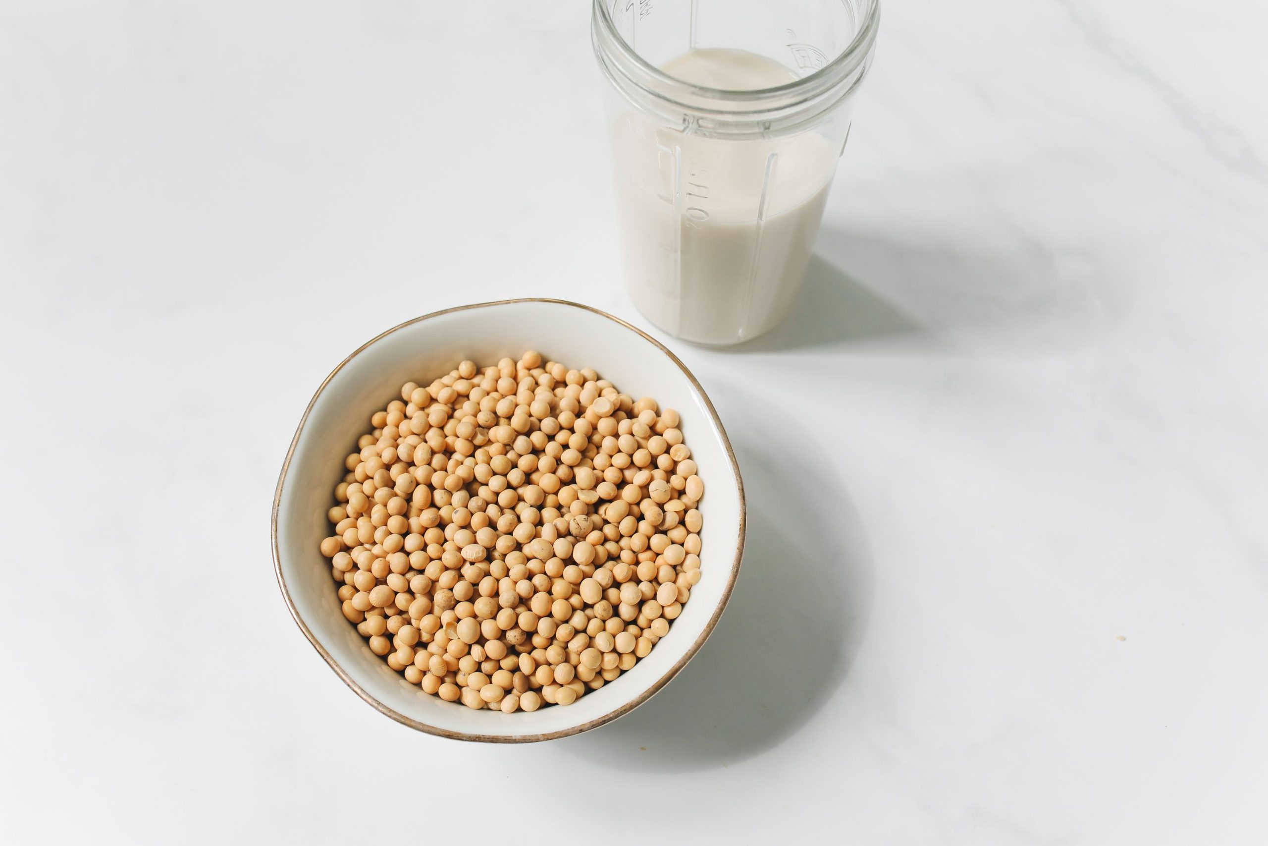 A bowl of soybeans and a glass of soy milk on a white background, showcasing healthy food options.
